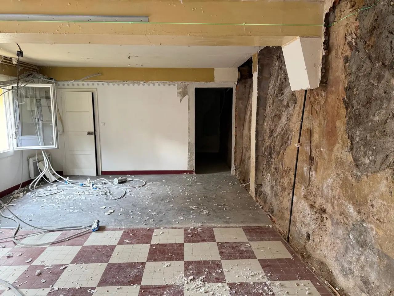 Pièce d’une maison ancienne avant travaux, murs mis à nu, gravats au sol, carrelage en damier