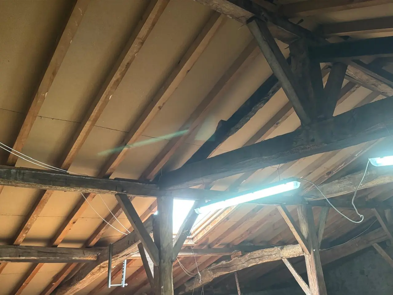 Avant : comble sous charpente ancienne, dessous de toiture nu, néons de chantier