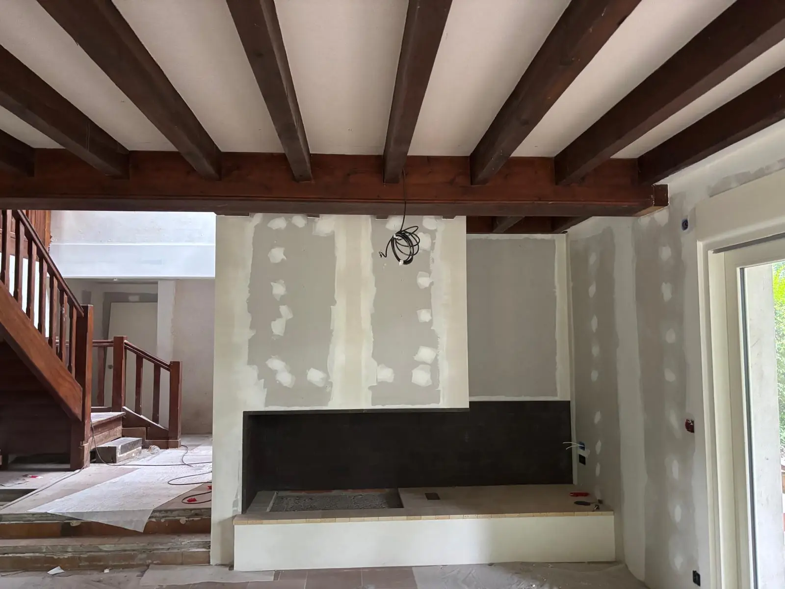 Séjour au plafond à poutres apparentes, cheminée habillée en plaques de plâtre aux bandes, escalier en bois