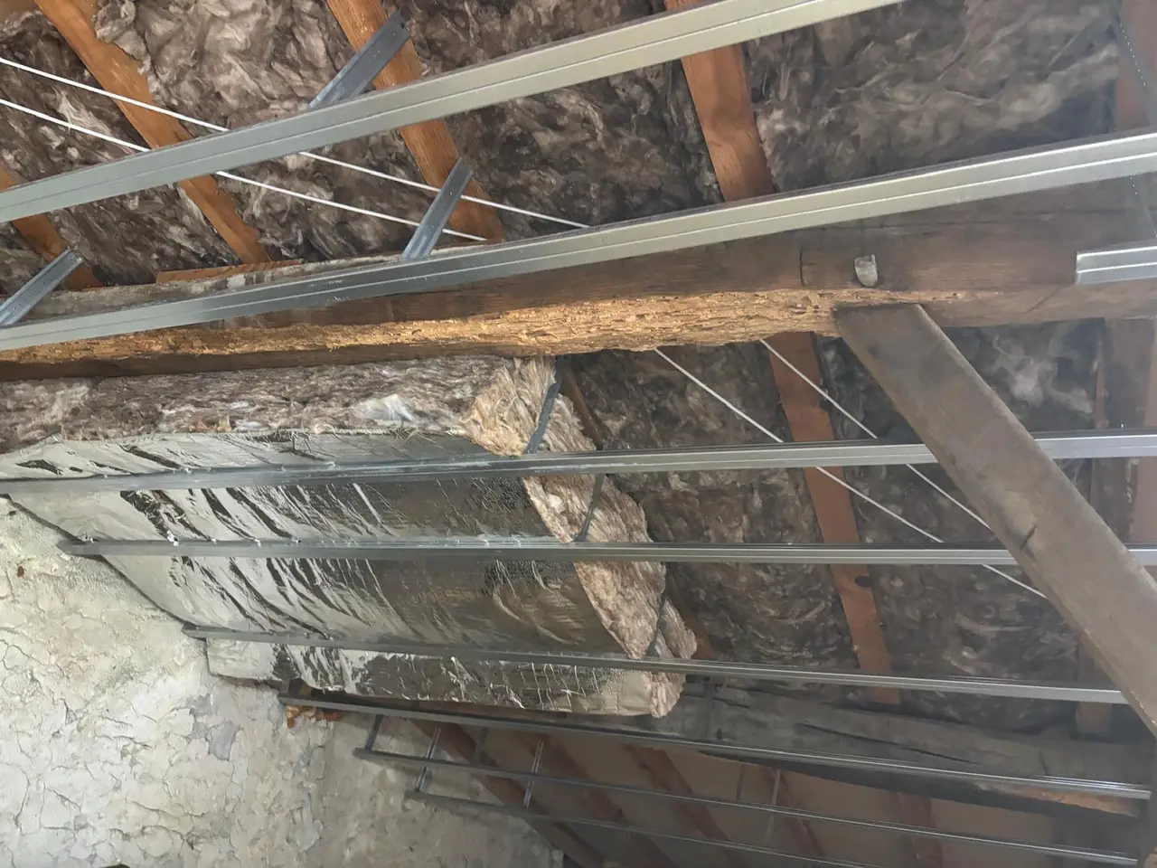 Rouleaux d’isolant entre les poutres d’une toiture, ossature métallique en cours de pose, mur de pierre