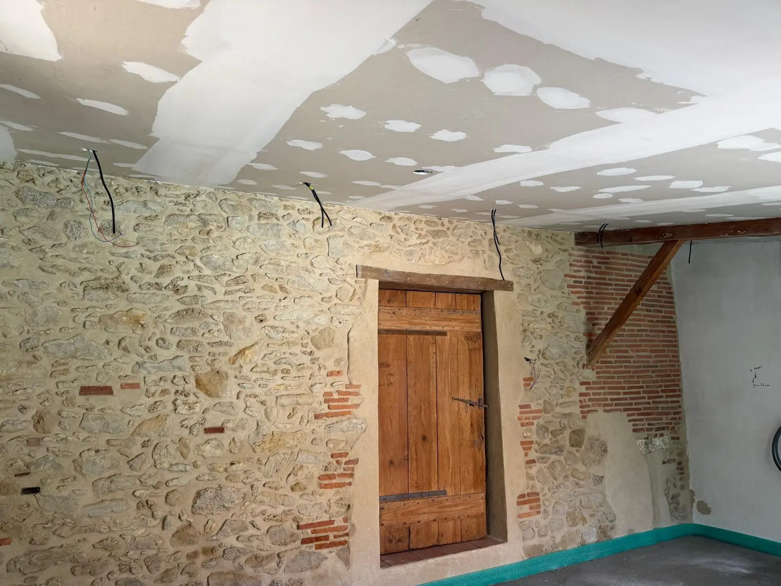 Plafond en plaques de plâtre aux bandes au-dessus d’un mur en pierre et briques apparent, porte en bois
