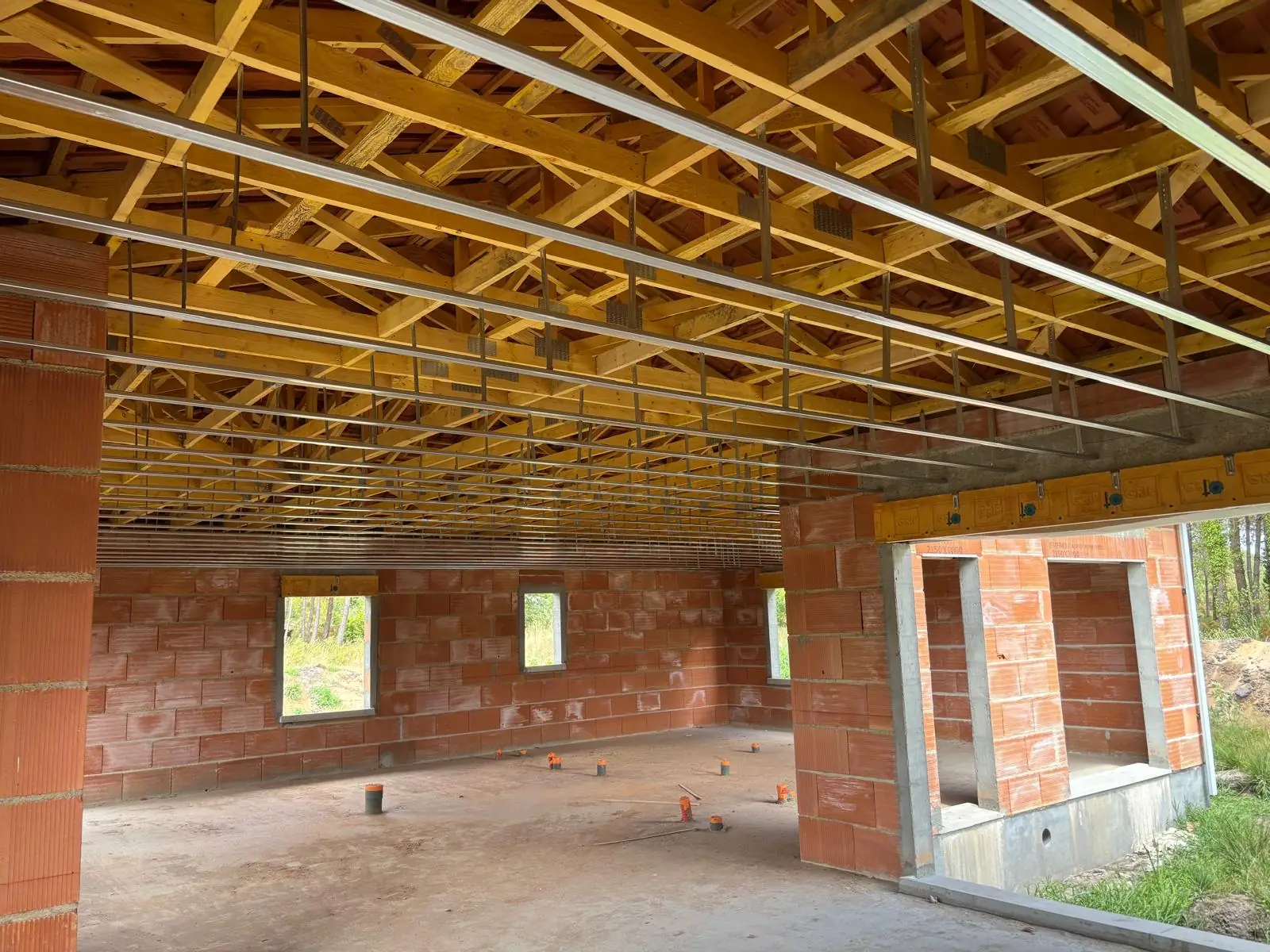 Ossature métallique d’un plafond suspendue sous une charpente en fermettes, maison neuve aux murs en briques