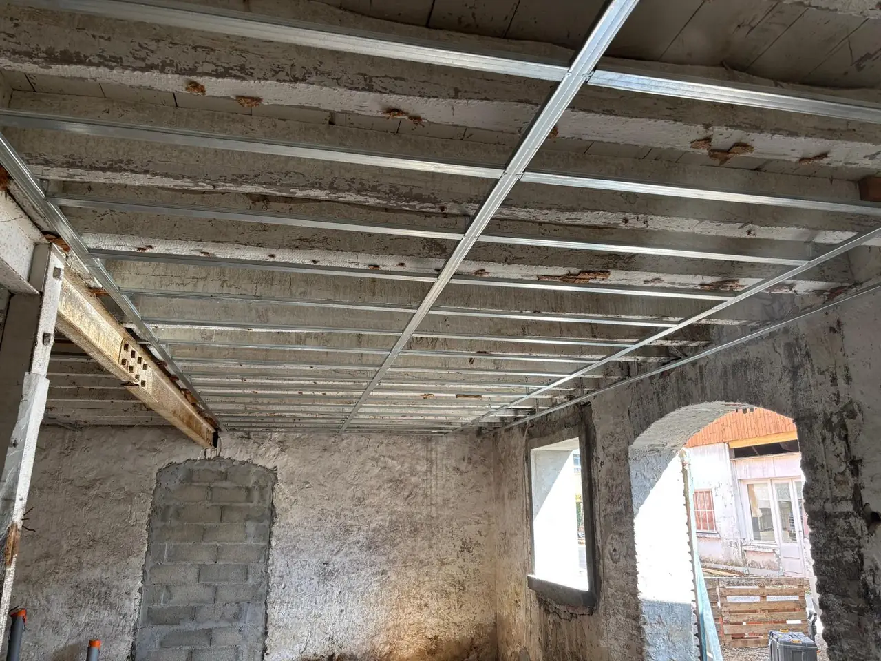 Ossature métallique de plafond suspendue sous un vieux plancher en bois, murs de pierre