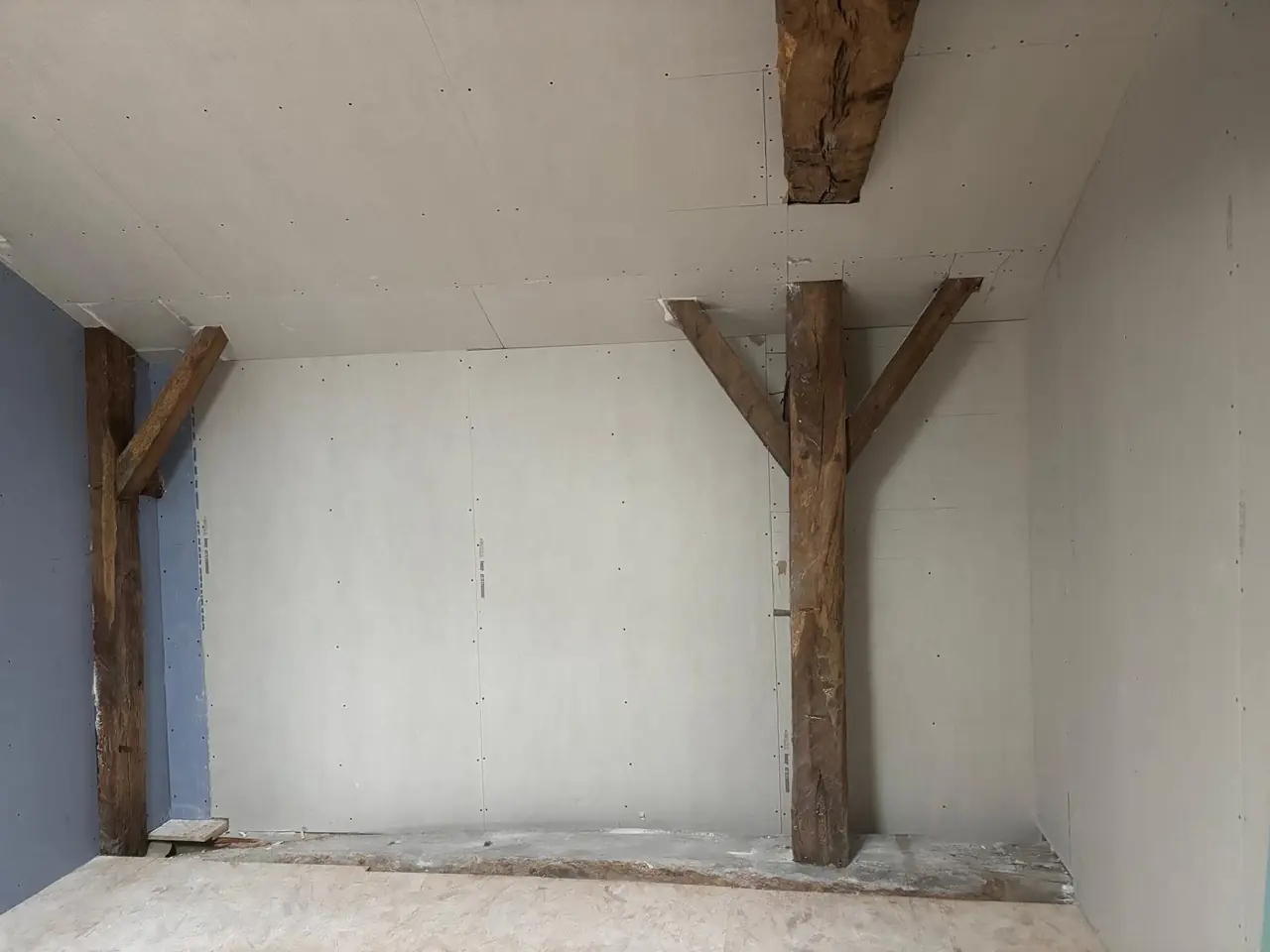 Mur en plaques de plâtre monté entre deux poteaux de ferme anciens en bois, avant les bandes